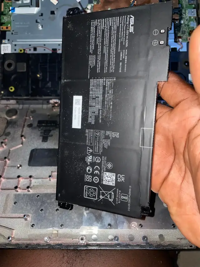 Replacement battery held over an open ASUS laptop